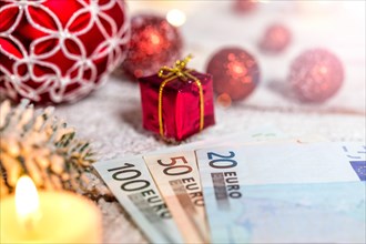 Christmas ball on old wooden table with candle and Euro banknotes